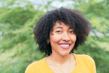 Portrait Smiling Latina woman looking at the camera while posing on a natural green background.