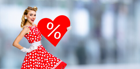 Woman holding red paper heart with % sign.  Portrait image of happy pin up girl. Blond model at...