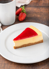 Delicious strawberry cheesecake with coffee next to it on wooden table