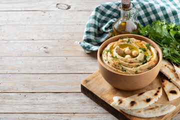 Chickpea hummus in a wooden bowl garnished with parsley, paprika and olive oil on wooden table....
