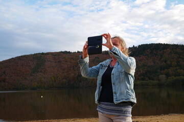 Fototapeta na wymiar Woman walks by a lake and takes a photo of the beautiful landscape