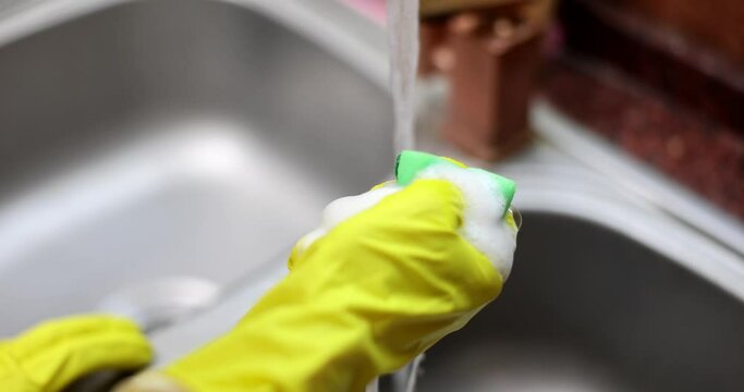 Hands of housewife in gloves squeezing sponge with soapy foam closeup 4k movie slow motion