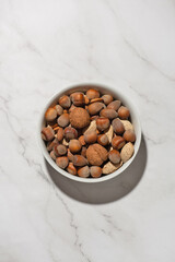 Different nuts in a white bowl on a gray table