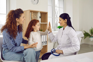 Smiling little girl child give high five to caring female pediatrician at visit to hospital with mom. Happy kid play make deal with doctor, enjoy good quality medical service. Children healthcare.