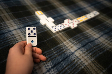 A child's hand with a white domino. A game of table dominoes with the whole family. Adding numbers...