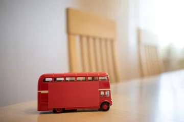 Fotobehang Een rode dubbeldekkerbus op de keukentafel. Een bus met een rode sticker aan de zijkant, een schone plek voor tekst. Het interieur van het meubilair in het appartement. Een tafel met stoelen op de achtergrond. © Svetliy