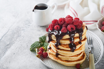 American pancakes. Stack pancakes with fresh raspberry with chocolate glaze or toppings in white bowl on light gray table background. Homemade classic american pancakes. Magazine concept. Top view.