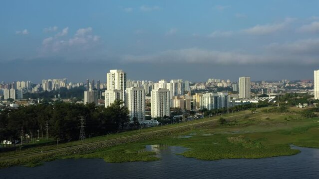 Aerial drone left trucking and panning shot of the south of S&atilde;o Paulo, Brazil from the man-made Guarapiranga Reservoir towards the Socorro neighborhood with skyscrapers and houses on a fall evening.