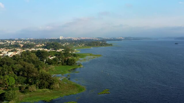 Beautiful rotating aerial drone shot of the man-made Guarapiranga Reservoir in the south part of S&atilde;o Paulo, Brazil with beaches, marinas, natural green ecosystems, and wildlife on a fall evening.