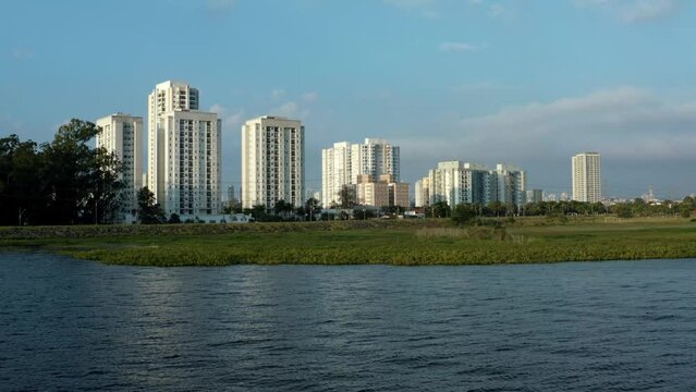 Aerial drone dolly-in shot of the Socorro neighborhood in the south of S&atilde;o Paulo, Brazil from the man-made Guarapiranga Reservoir with calm waters and skyscrapers in the background on a fall evening