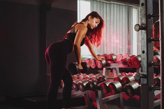 Fitness girl is doing exercises with a dumbbells in a gym