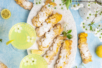 Eclairs with lemon curd topping on serving plate with glass of limoncello on a light background,...