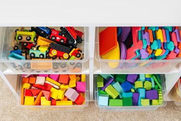 Transparent plastic storage boxs on shelves. White shelving with rainbow wooden toys in plastic...