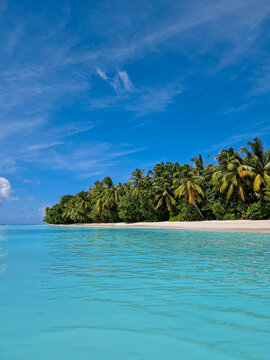 Eine Insel mit menschenleerem Strand, Palmen und t&uuml;rkis blauen Wasser mit seichten Wellen auf einer traumhaften Insel auf den Malediven (Hochformat)