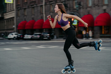 Horizontal shot of active slim young woman rides fast on rollerskates improves balance agility and...