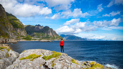 A beautiful girl stands on the rocks above the sea overlooking the mighty mountains on the lofoten islands in norway; the mighty norwegian fjords