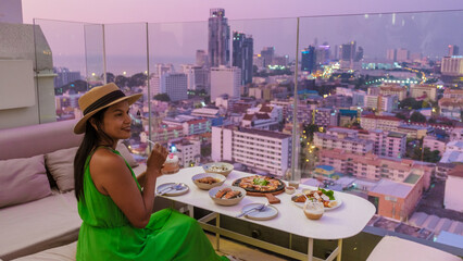 young Thai women having a drink on a rooftop bar looking out over the city