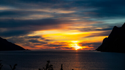 colourful sunset reflected in the water surrounded by mighty mountains in the norwegian fjords, senja island, norway