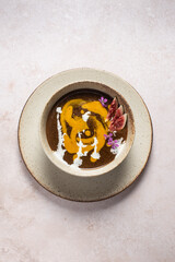 traditional Latvian sweet rye bread soup with pumpkin and cream decorated with fig and flowers on light beige table