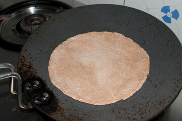 cooking round roti on tawa with the Dough of Ragi Nachni or finger millet flour. It is also use to...