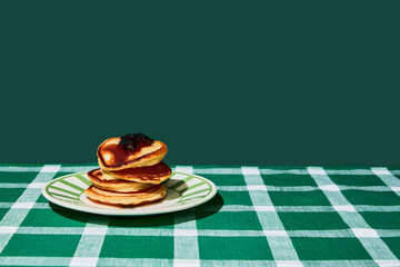 Plate of delicious sweet pancakes with jam on green tablecloth over green background