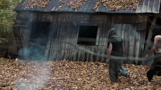Two mysterious men wearing atypical costumes walking to a rustic cabin.
