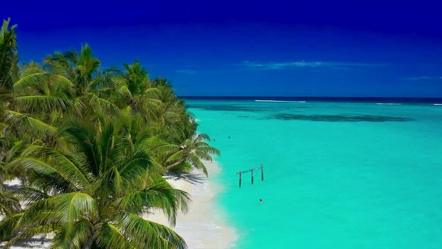 Paradise white sand beach, turquoise ocean, green palm trees and blue sky with clouds on a sunny day in island Thoddoo in Maldives. Summer tropical landscape, aerial panoramic view.