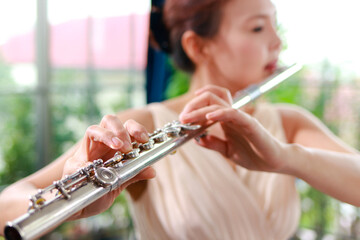 Asian woman wearing a cream colored dress She is playing the flute, an international wind instrument. Play classic songs. Performing concerts playing classical music in a band. music learning