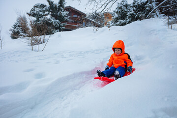 Fototapeta na wymiar Happy boy in orange ski sport outfit go downhill on the sledge