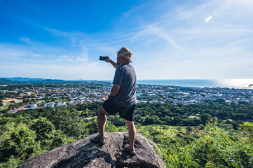 Obraz premium Asian fat man stand on the rock and take photo at Khao hin lek fai view point.Khao Hin Lek Fai is a place to see a spectacular view of the entire town.Also know as khao radar in local people.