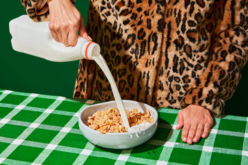 Woman pouring milk into plate with cornflakes on green tablecloth. Time for breakfast
