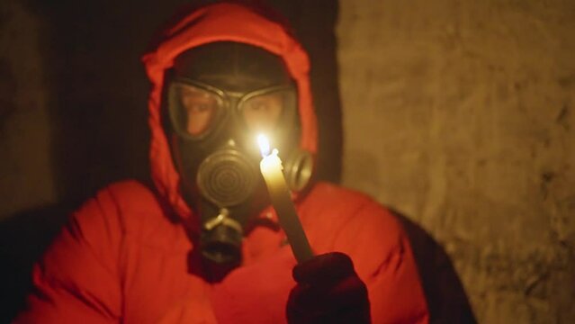 Ukraine war. A young man in a gas mask hides in a bomb shelter from rocket fire; there is no electricity, he lights a candle