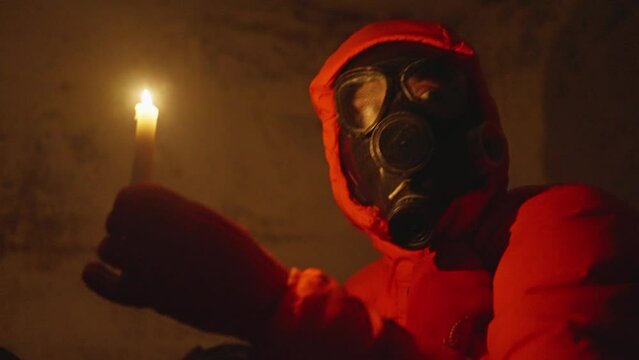 Ukraine war. Shelter. Bunker, nuclear war, a man in a gas mask and protective clothing is hiding in a bomb shelter, electricity is turned off, a man is lighting a candle, he is scared