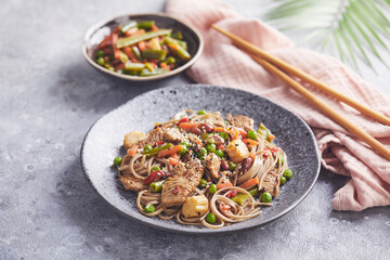 Wok with turkey meat, soba noodles, corn, green peas, green beans and carrots served on gray background with chopsticks. Asian food, concept of street food