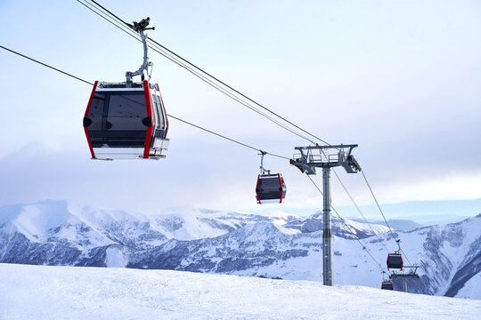 Cable car gondola at ski resort with snowy mountains on background. Modern ski lift with funitels and supporting towers high in the mountains on winter day. No people.
