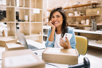 Happy online store owner using a smartphone in a warehouse