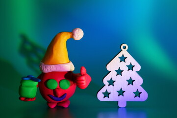 A virus figurine in a New Year's hat and with a gift on a green background.  Next to the Christmas tree. Festive decorations.