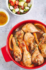 Chicken drumsticks with oranges and thyme baked in red round baking dish
