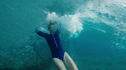 Woman surfer dives underwater in front of the approaching wave. Shaky camera after hit of the wave