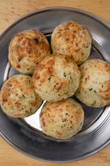Street South American food. Closeup view of small, baked, cheese-flavored rolls, called chipa, in a metal dish with a wooden background.