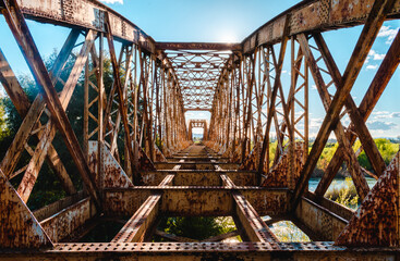 Vista central desde dentro de Puente metálico de tren o ferrocarril abandonado, oxidado y antiguo, con luz del sol al medio día con vegetación al rededor