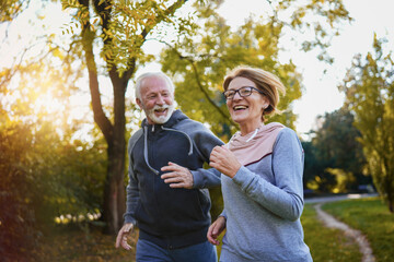 Cheerful active senior couple jogging in the park. Fitness routines for elderly people. Working out together. Exercise to stop aging. 