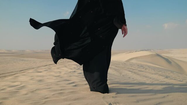 Close-up of girl in traditional Abaya dress walking barefoot along the dunes in the desert of Doha Qatar. 4K Slow Motion
