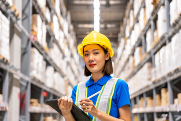 Beautiful asian engineer woman wearing safety helmet and reflective vest, She checking goods supplies on shelves with tablet in ware house and looking camera. Logistic and business export concept.
