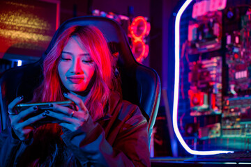 Fototapeta na wymiar Young woman live stream she play video game at home neon lights living room, Gamer playing online game application on mobile smart phone wear gaming headphones, E-Sport concept