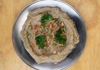 Middle Eastern cuisine. Closeup view of traditional baba ganoush spread, made with pureed aubergines and sesame seeds, in a metal dish on the wooden table.