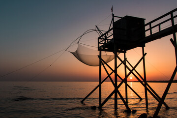 Fototapeta na wymiar cabanes de pêche sur pilotis en Loire Atlantique appelées pêcheries face à l'océan et au soleil couchant
