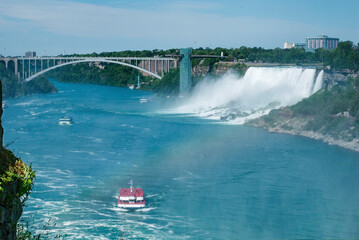 Niagara falls and Niagara river in Canada, Ontario. Three tourist boats sail on the Niagara river. In the background is a bridge between the Canadian and American border.