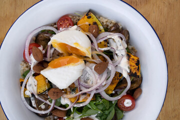 Healthy food. Top view of a gourmet salad with sliced cabbage, roasted eggplant, red onion, almonds, arugula, pumpkin and a poached egg in a white bowl.