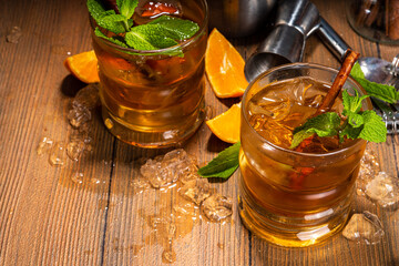 Autumn spicy booze alcohol drink, Tangerine Whiskey Smash cocktail with mint, cinnamon and tangerine slice on wooden background